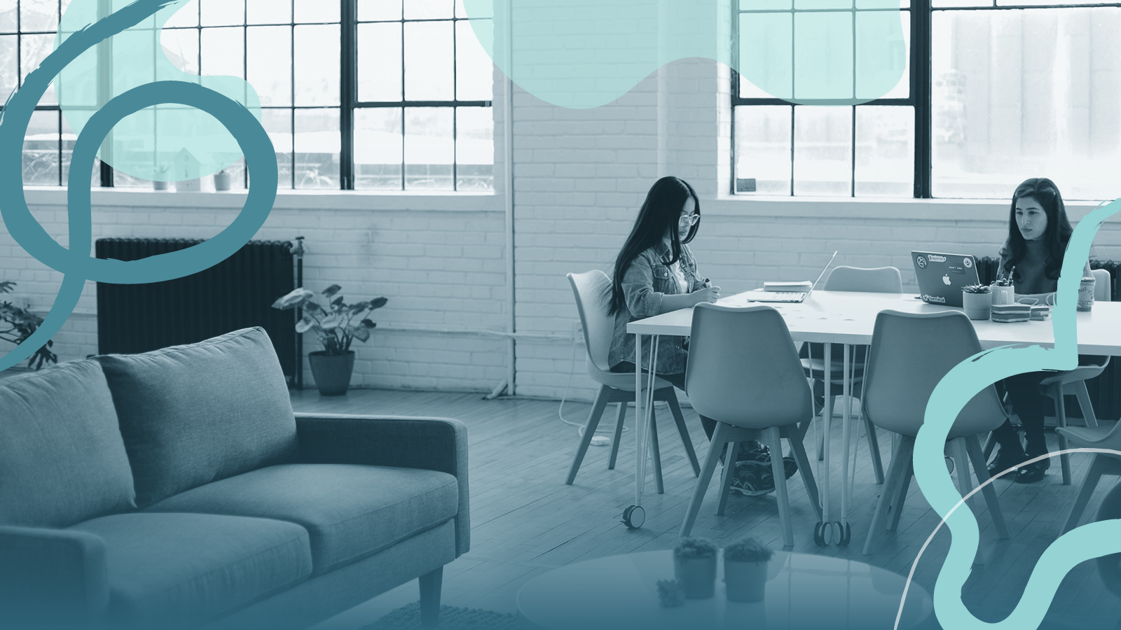 Two young women working at a large meeting desk in a modern office space.