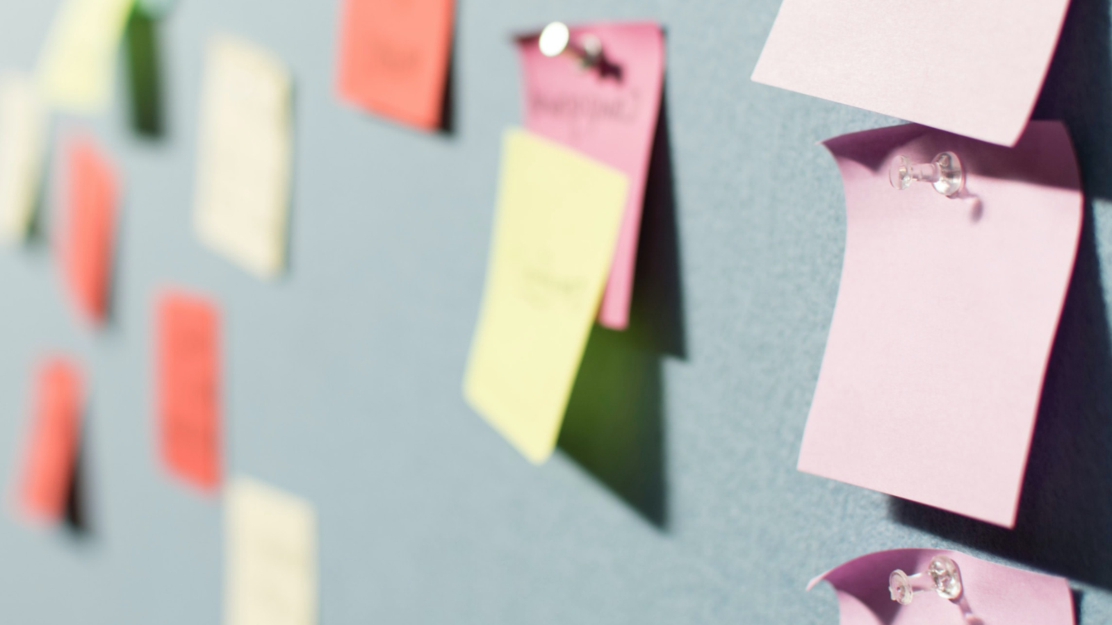 A closeup of a wall with many colored notes pinned to it.